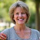 Elizabeth, a woman in her late 40s, smiling confidently while holding a smartwatch. She looks active and healthy, perhaps after a brisk walk.