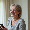 Maria, a woman in her early 60s, smiling warmly while holding a tablet or smartphone, perhaps showcasing a health app. She appears vibrant and engaged.